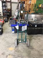 Front view of green metal hand truck with large wheels and foldable toe plate in a warehouse setting