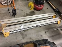 Metal portable saw tables stacked or folded on a concrete floor with some tools and equipment in the background.