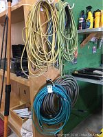 Yellow and green extension cords hanging on a wooden stand with workshop shelves in background.