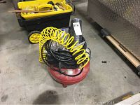 Photo of red Porter Cable air compressor with yellow coiled hose and black cables on top, set on concrete floor.