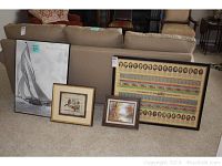Four framed artworks placed on and in front of a beige couch, including a large US Presidents poster, a large black and white sailboat photo, and two smaller framed pictures (one a landscape print, one possibly an oil painting).