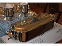 Rectangular stainless steel fish poacher with polished finish and fish-shaped handle on lid, shown with two pewter tankards in background