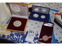 Four coin lot including 2008 Beijing Olympic commemorative medallion in yellow case, 1984 Los Angeles Olympics coin set in blue case, and two US Liberty coins in red case.
