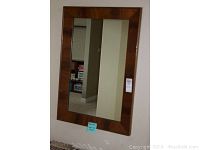 Full view of the rectangular mirror mounted on a wall with wood frame.