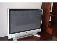 Front and side view of the Panasonic flatscreen TV on a wooden surface, showing its silver finish and base stand.