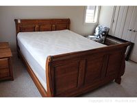 Sleigh bed frame with warm brown wood finish and curved headboard and footboard visible from an angle, sitting on carpeted floor.
