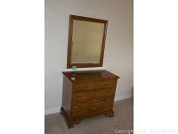 Dresser with mirror positioned above it in a room with beige carpet and walls.