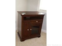 Front angle view of the wooden TV cabinet showing one drawer, open shelf, and side door storage compartment with metal knobs and glass-front door.