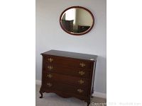 Wooden dresser with four drawers, ornate brass handles, and decorative legs.