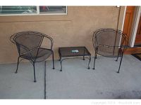 Photo of the full patio set showing two chairs and one small table arranged against an exterior wall on concrete.