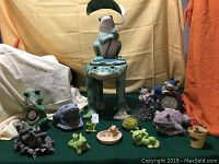 Full lot of various garden frog decorations on green cloth, includes large frog statue with leaf umbrella and various smaller frog figurines and planters