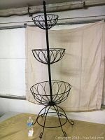 Full view of black wire basket stand with three tiers showing sizes of baskets and base support.
