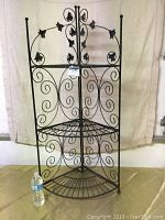 Front view of the 3-tier black metal wire corner stand showing scrollwork and leaf design on back panel and triangular shelves.