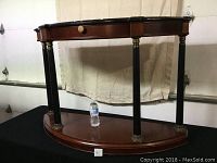 Front view of demi lune side table showing single drawer with wooden knob and black tapered legs with gold accents.