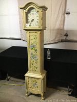 Full frontal view of the tall vintage-style standing clock with cream-colored case and blue floral designs.