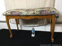 Full view of solid wood piano bench with floral upholstered padded seat and cabriole legs