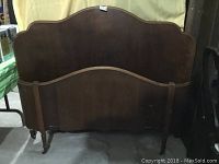 Front view of the tall, dark stained solid wood headboard with curved top edge and caster wheels on turned legs.