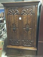 Full frontal view of the large wood veneer armoire showing two paneled doors with ornate carvings and a bottom drawer.