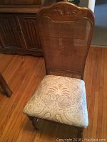 Front view of an oak dining chair with caned back and upholstered seat in patterned fabric, carved detail on the top of the backrest.