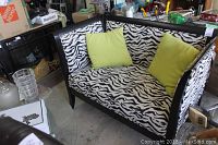 Front view of loveseat with zebra print upholstery, green pillows, and black wooden frame.