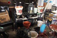 Metal shelving unit with various flower pots and garden accessories arranged on it, including white ceramic pots with poinsettia patterns and black plastic or ceramic pots