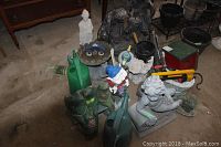 Wide angle photo showing the fountain, statues, garden gnome, watering cans and other garden decor items clustered together on ground.