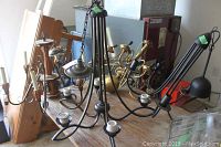 Photo showing the modern style black metal chandelier with multiple arms alongside at least two other metal chandeliers on a wooden surface.