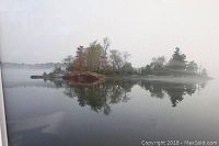 Close-up photo of island on lake art print showing the scene with tree-covered island and its reflection on calm water in a misty setting