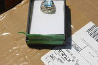 Aquamarine ring placed in an open small black jewelry box with white cushion, resting on a cardboard box with label partially visible.