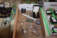 Wide view of lot showing multiple watches, sterling charm bracelet, brooch, rings, and other jewelry items spread on tan cloth.