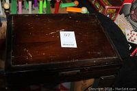 Closed dark wood canteen box for silverware storage with scratch marks and hinge broken on one side.