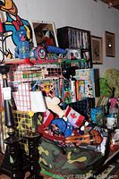 Wide view of shelf with assorted VHS tapes, DVDs, toys including Mickey Mouse items and a jar of marbles, plus a camouflage bag with various toys.