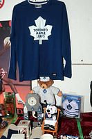 Blue long-sleeve shirt with Toronto Maple Leafs logo, mini jersey in box, stuffed bears, and clock.