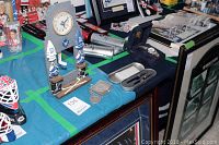 Full view of resin clock, key chain, medallion, pen set case, and watch box with watch inside. Displayed on blue table cloth with other collectibles visible in background.