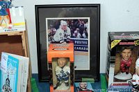 Collection showing framed photo of Mats Sundin, hand-painted bobblehead in original packaging in Maple Leafs uniform, and other memorabilia items on table