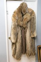 Front view of full men's coyote fur coat hanging on door showing length and shoulder width.