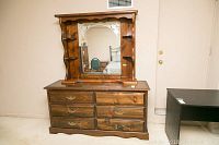 Front view of vintage wooden dresser with mirror, showing six drawers, dark wood, missing drawer pulls, scratches on surface, and etched decorative corners on mirror.