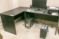 Photo showing one of the black L-shaped desks with computer monitor, printer, and computer tower underneath