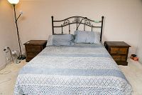 Pair of wooden night tables flanking a bed with blue bedding and metal headboard, floor lamp and power cords to left