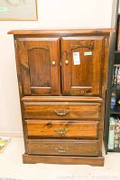 Front view of the wooden highboy/tallboy cabinet showing two upper cabinet doors and three lower drawers with metal handles.