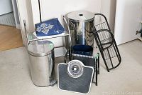 Photo showing two metal garbage cans, Starfrit balance scale, metal wall hanging rack, black storage rack, and blue cloth.