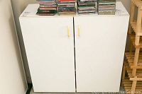 Front view of two white cabinets side by side with gold handles, visible signs of wear and items on top of cabinets.