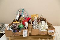 Wide view of two boxes filled with various Christmas decorations including glass trees, ornaments, candy dish, plates, and other holiday items on pallet
