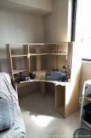 Photo showing the light brown melamine corner computer desk with shelving unit and storage compartments, placed near a window and wall.