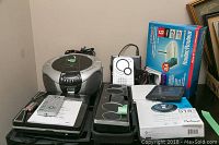 Wide shot showing all electronic items including boxed Air Plus router, silver and black Magnasonic CD player, and other portable players on a table.