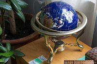 Globe displayed on wooden surface near plants and window, showing overall item.
