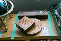 Three lacquered decorative boxes arranged on a table: one elongated rectangular box with a fine pattern, one square box with ribbed top, and one round box with geometric design.