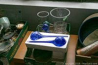 Two clear glass vases and a clear glass bowl behind a box containing a pair of blue glass water bulbs, with parts of other items visible