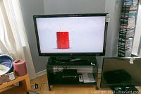 Front view of the Westinghouse TV on black stand with electronics below and remote control on stand