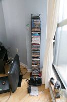 Photo of the black metal DVD and Blu Ray stand filled with a large collection of DVDs and Blu Ray discs, standing next to a TV and other electronics.